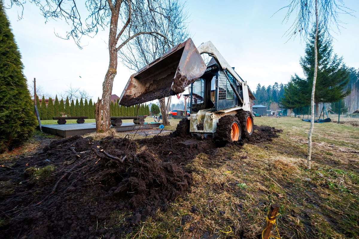 Compact loader with its bucket carving a graded trench for a new driveway